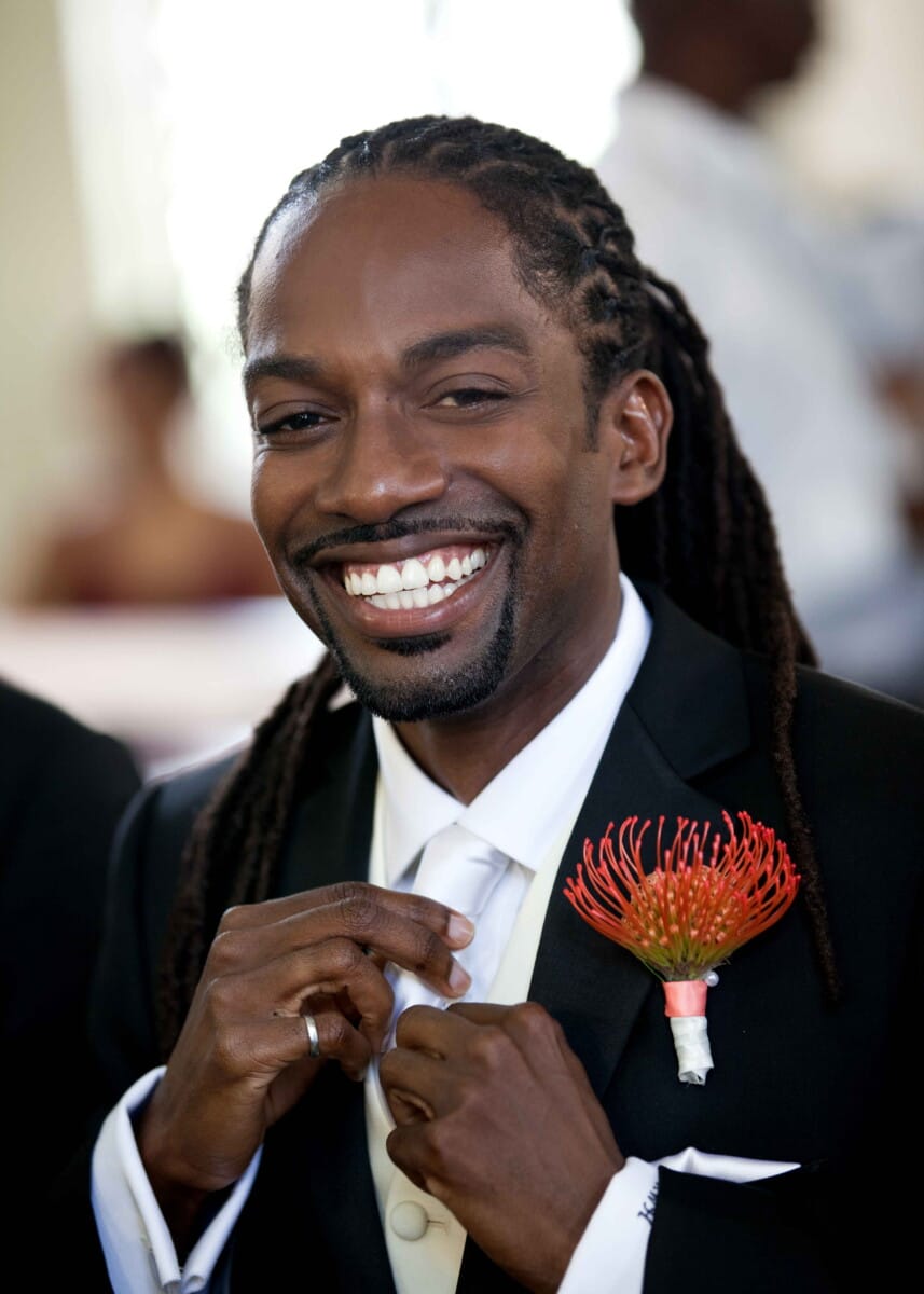 Smiling groom adjusting his tie with a tropical boutonniere