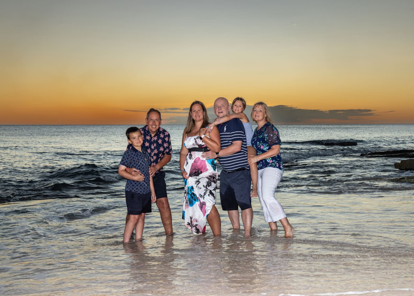 Family standing together in the sea at sunset in Barbados