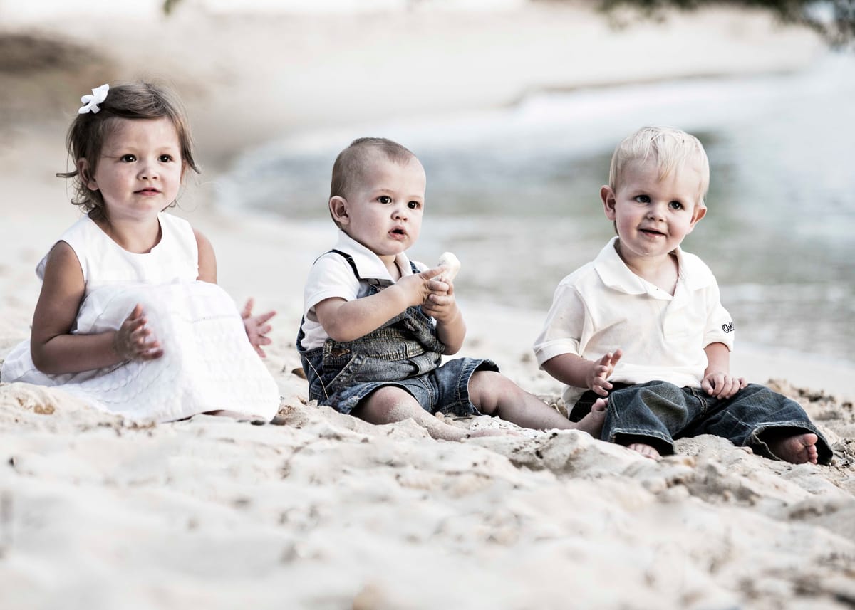 Three young children seated together on a Barbados beach