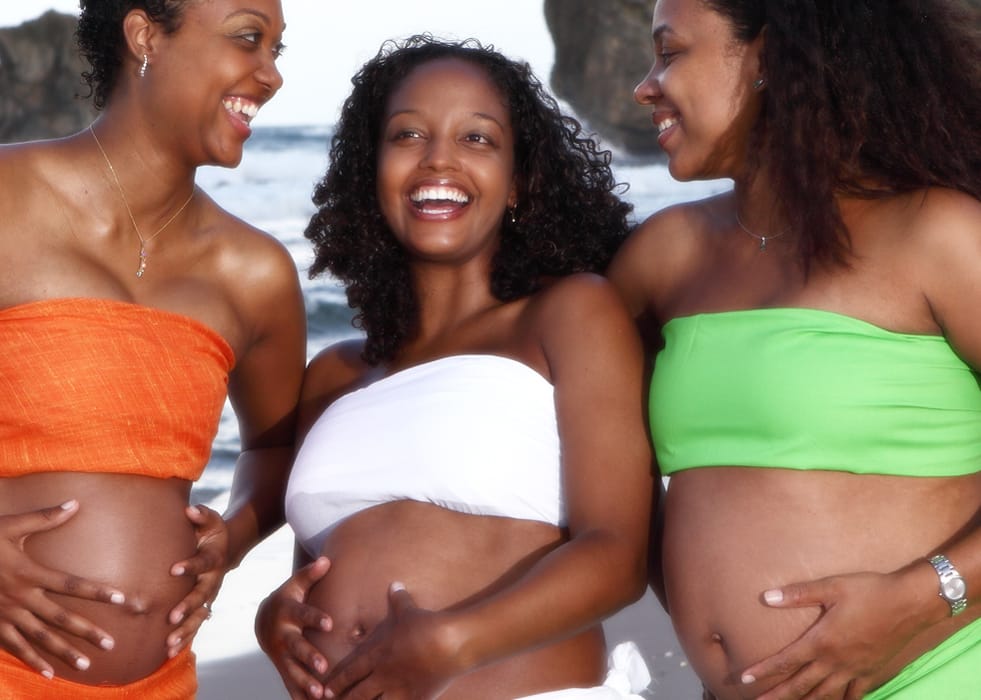 Three expectant mothers smiling together during a beach maternity session