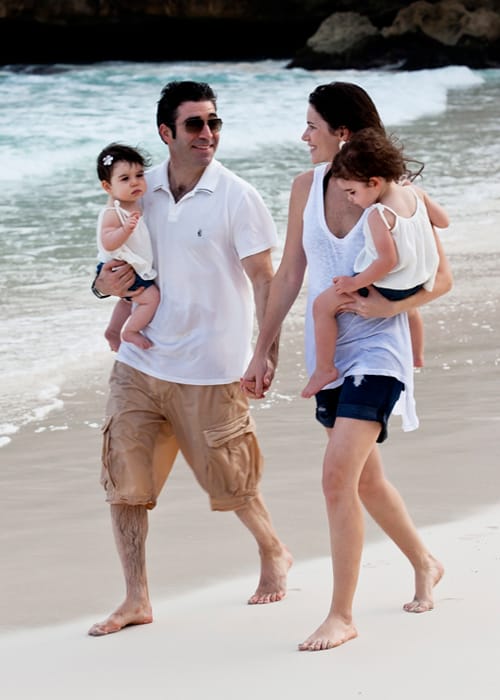 Parents carrying their young children while walking on a Barbados beach
