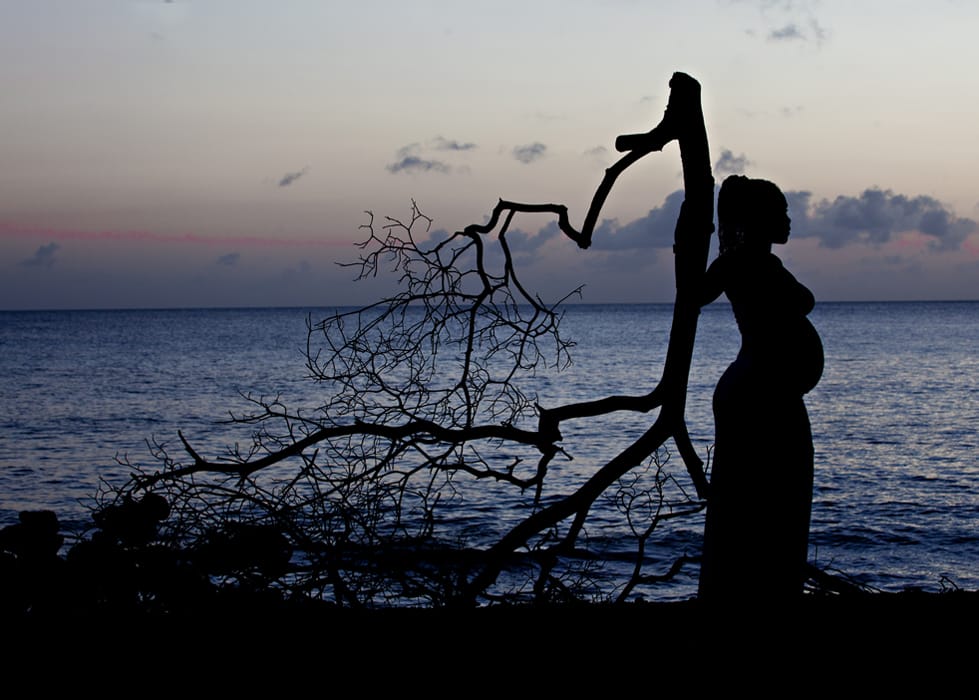 Silhouette of an expectant mother beside the sea at sunset in Barbados