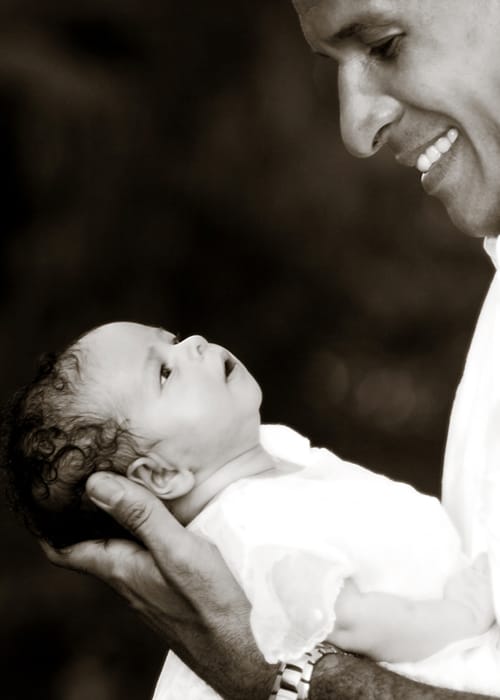 Father smiling at his newborn baby in a black-and-white family portrait