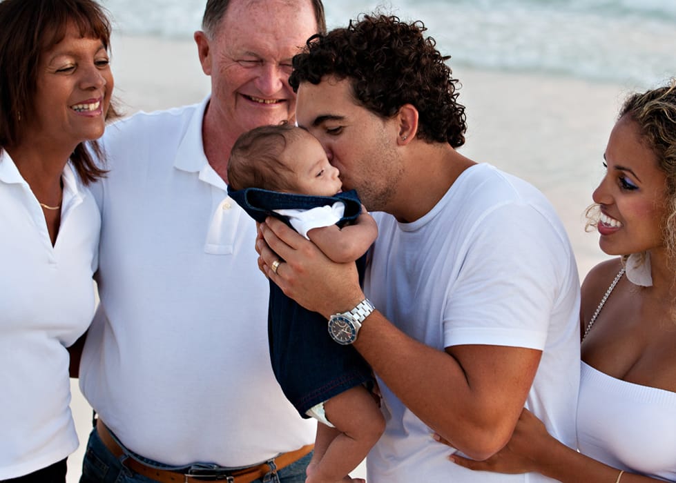 Father kissing his baby while grandparents and mother smile nearby