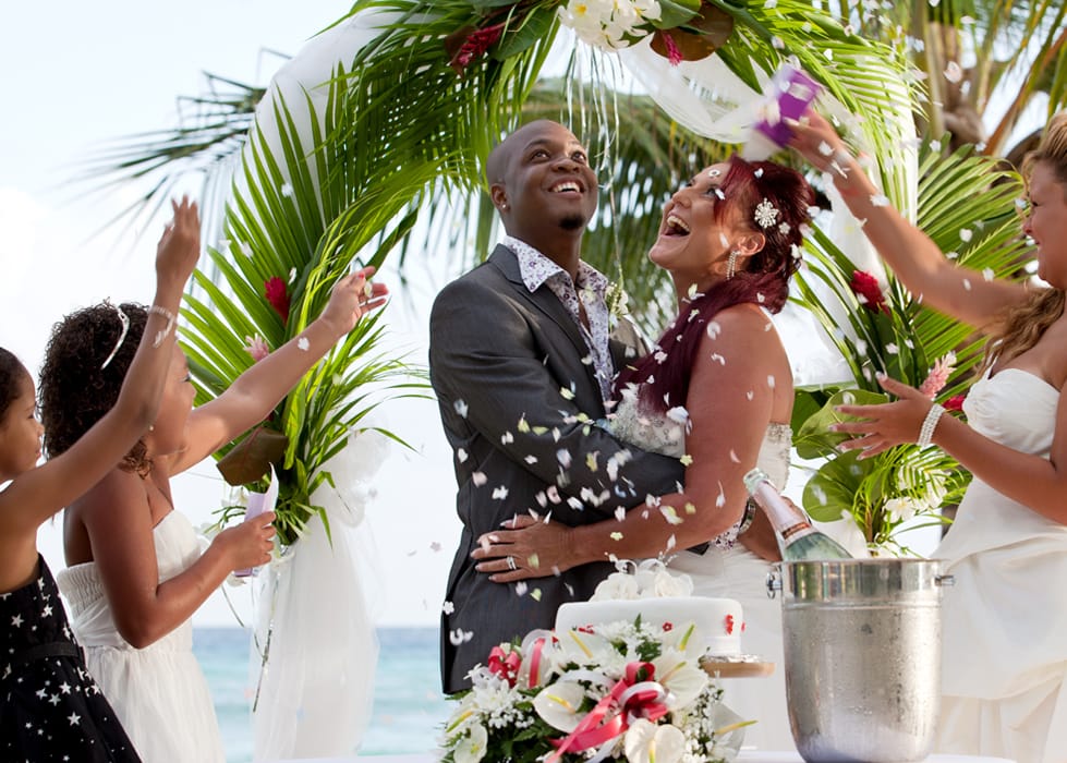 Newlyweds laughing as guests toss flower petals at their beach wedding