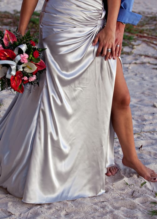 Bride holding a tropical red bouquet beside the groom on a sandy beach