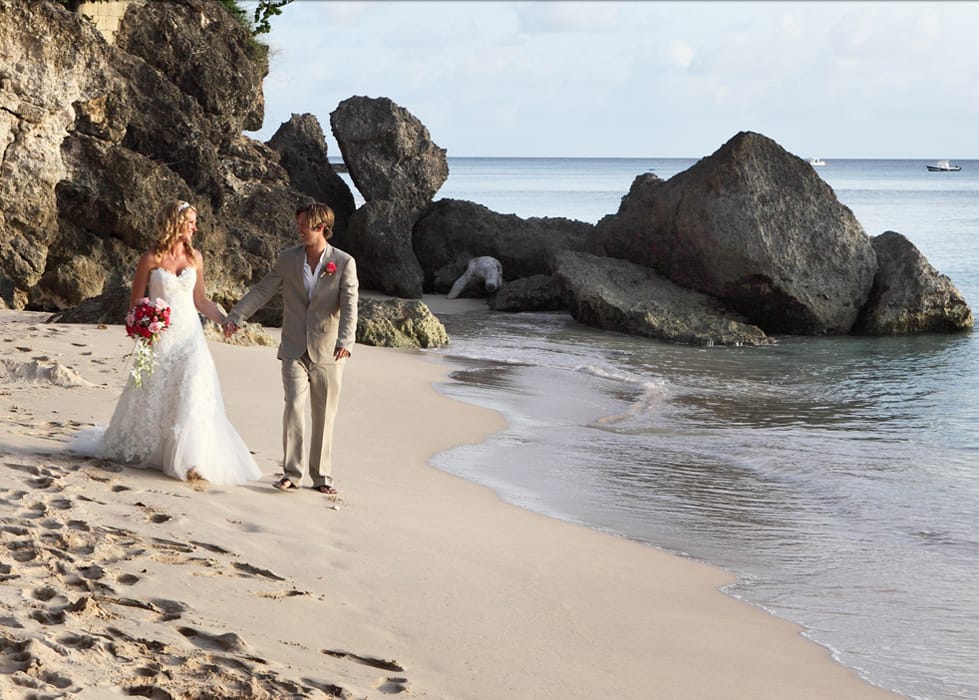 Newlyweds walking hand in hand beside the rocks on a Barbados beach
