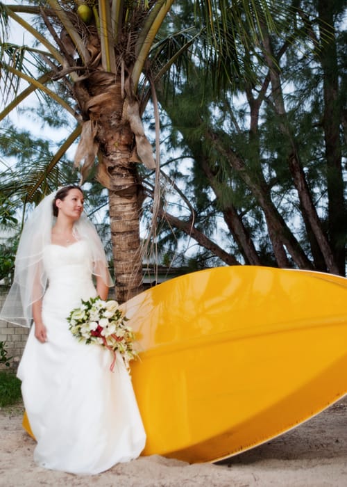Bride standing beside a bright yellow boat beneath a palm tree
