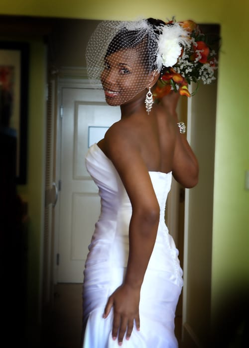 Bride posing in her wedding dress with a birdcage veil and tropical flowers