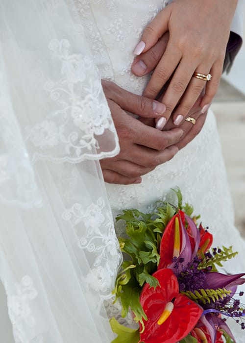 Close-up of the bride and groom showing their wedding rings and tropical bouquet
