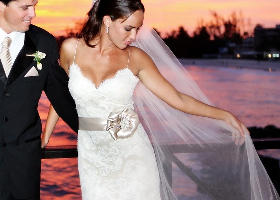 Bride arranging her veil beside the groom during a colorful sunset portrait