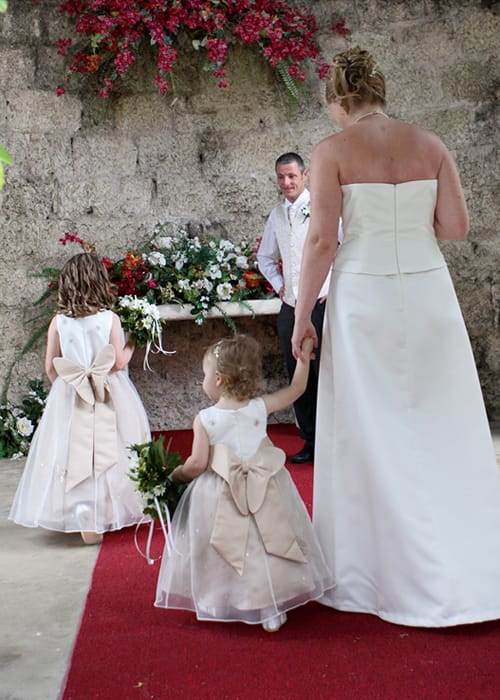 Bride walking down the aisle with two young flower girls toward the groom