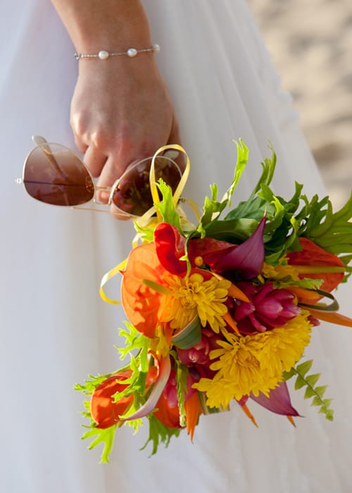 Bride holding sunglasses and a vibrant tropical wedding bouquet