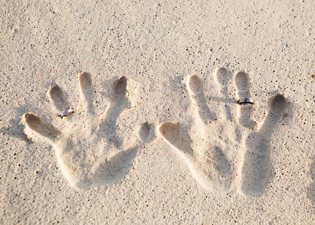 Family handprints and wedding rings pressed into Barbados beach sand