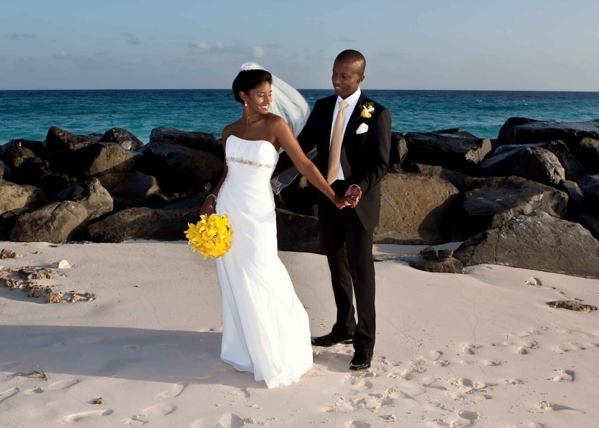 Newlyweds holding hands beside the rocks and turquoise sea in Barbados