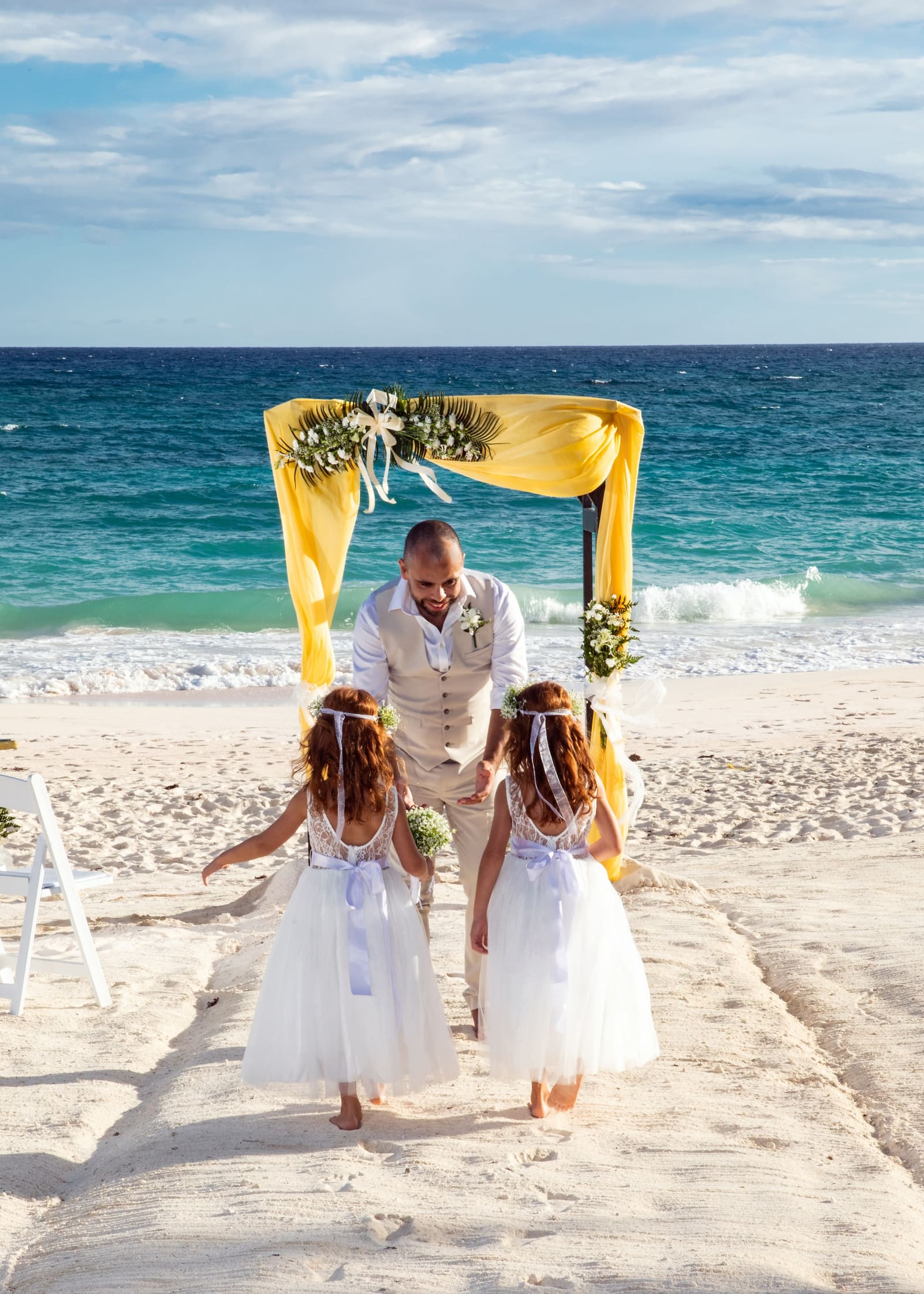 Bride and groom with two flower girls at a yellow beach arch, Barbados