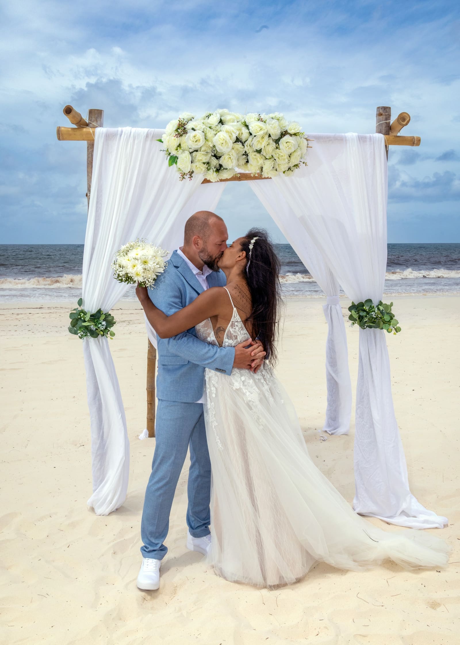 Couple kissing under a white floral beach arch, Barbados