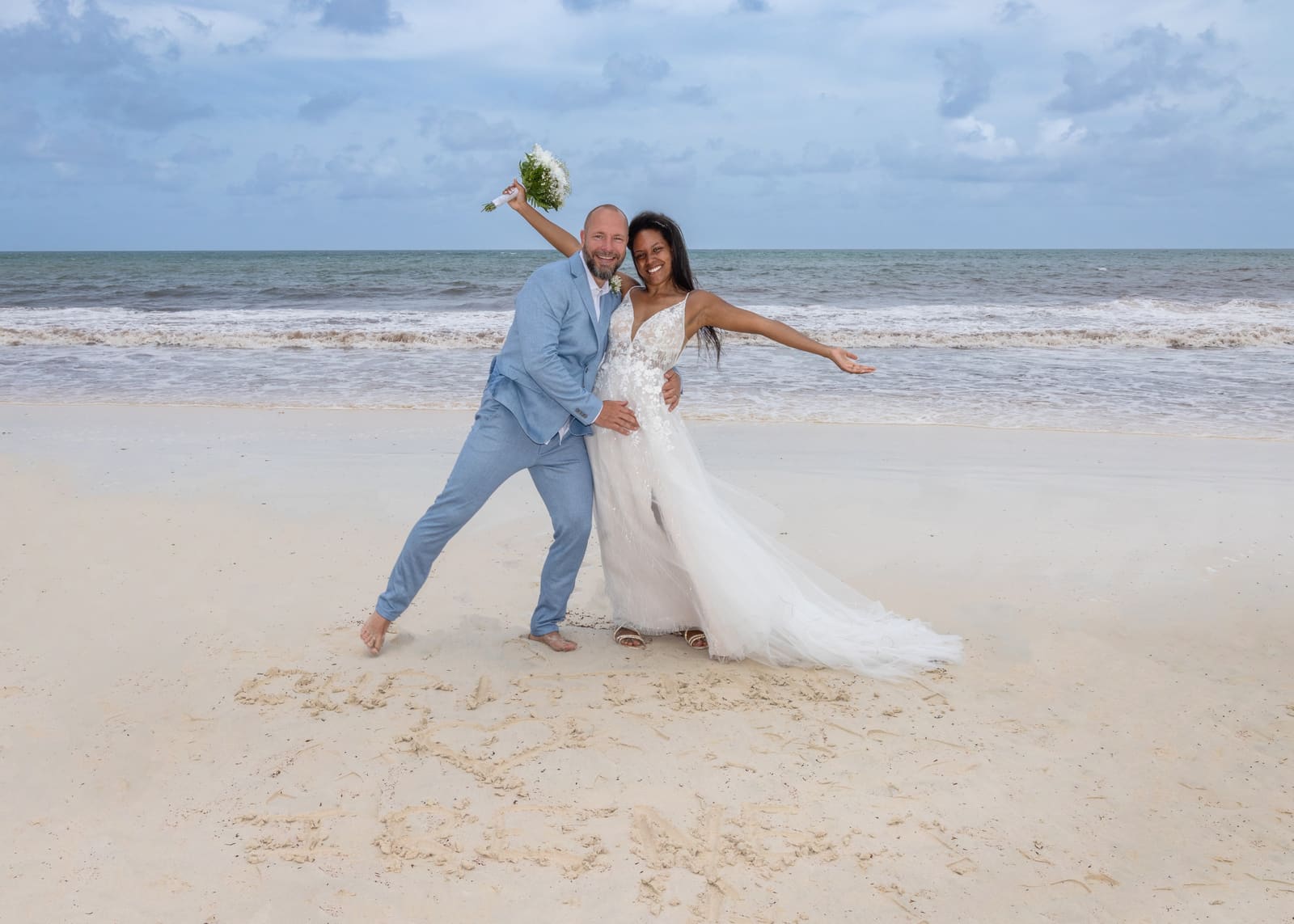 Couple celebrating on the beach beside a message drawn in the sand, Barbados