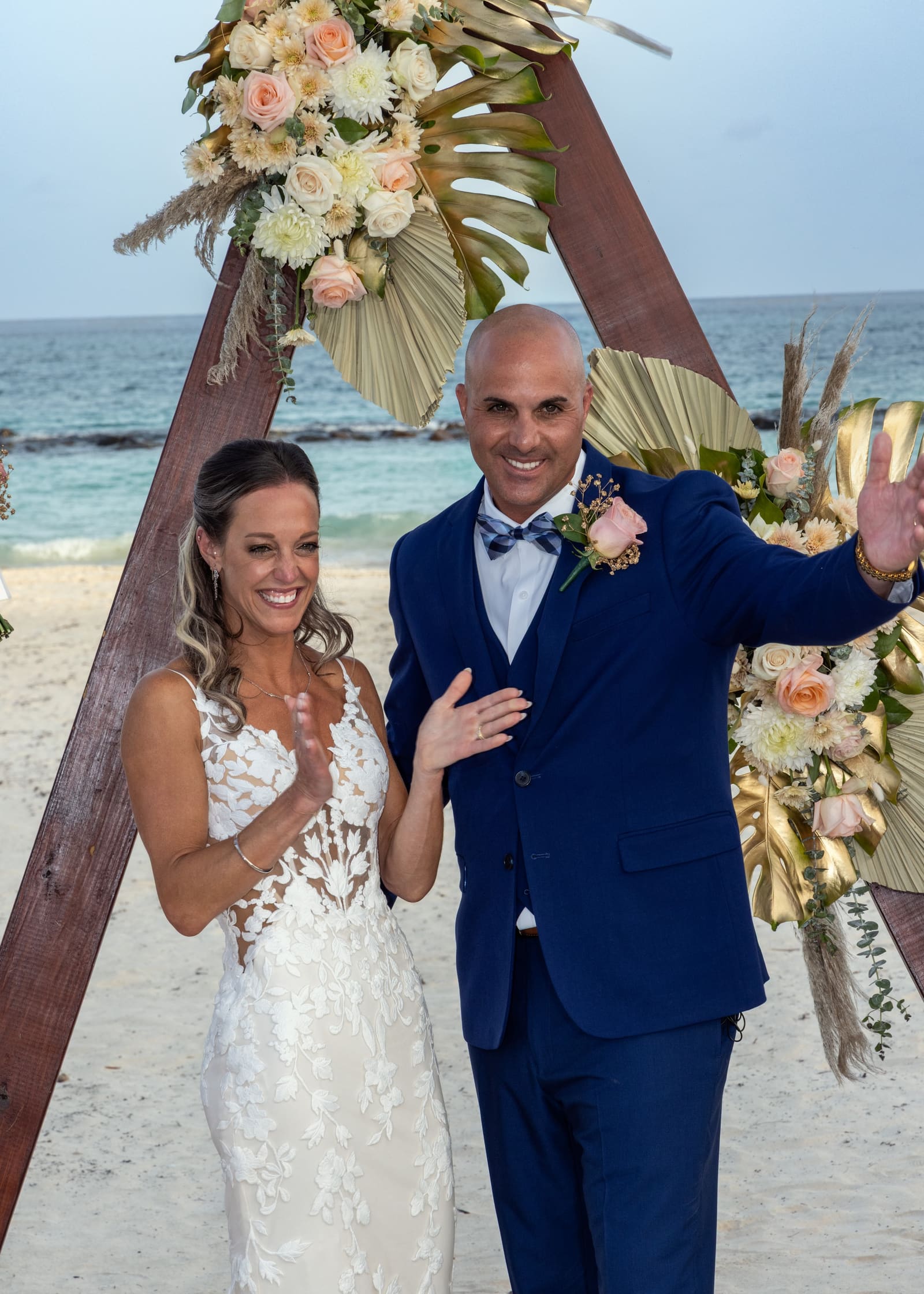 Bride and groom celebrating beneath a floral beach arch, Barbados