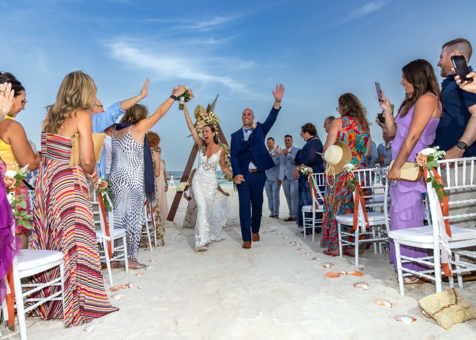 Guests cheering as the newlyweds walk back up the aisle on the beach, Barbados