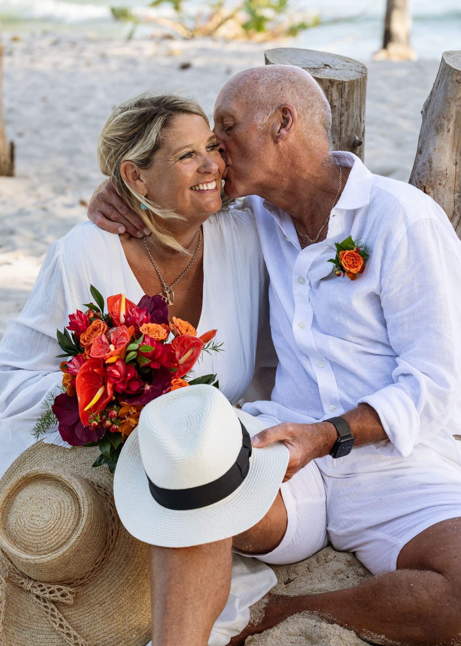 Couple laughing on the beach with a bouquet and a straw hat, Barbados