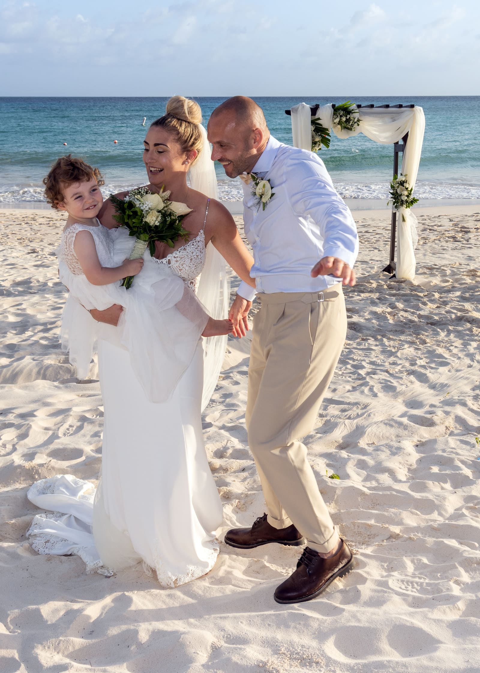Groom dancing on the beach as the bride holds a child, Barbados