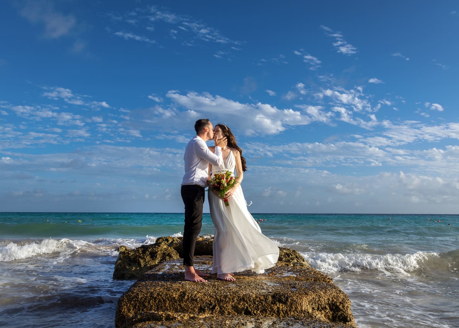 Couple kissing on a rock in the sea, Barbados