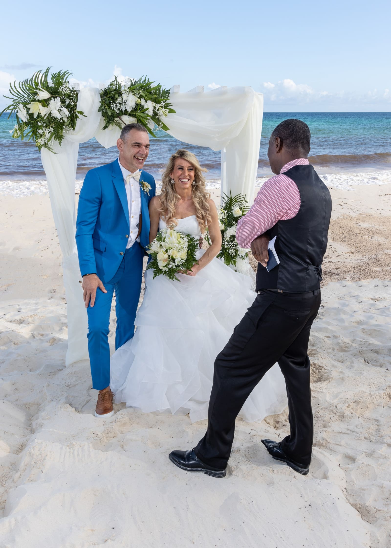 Couple laughing with the officiant at a beach arch, Barbados